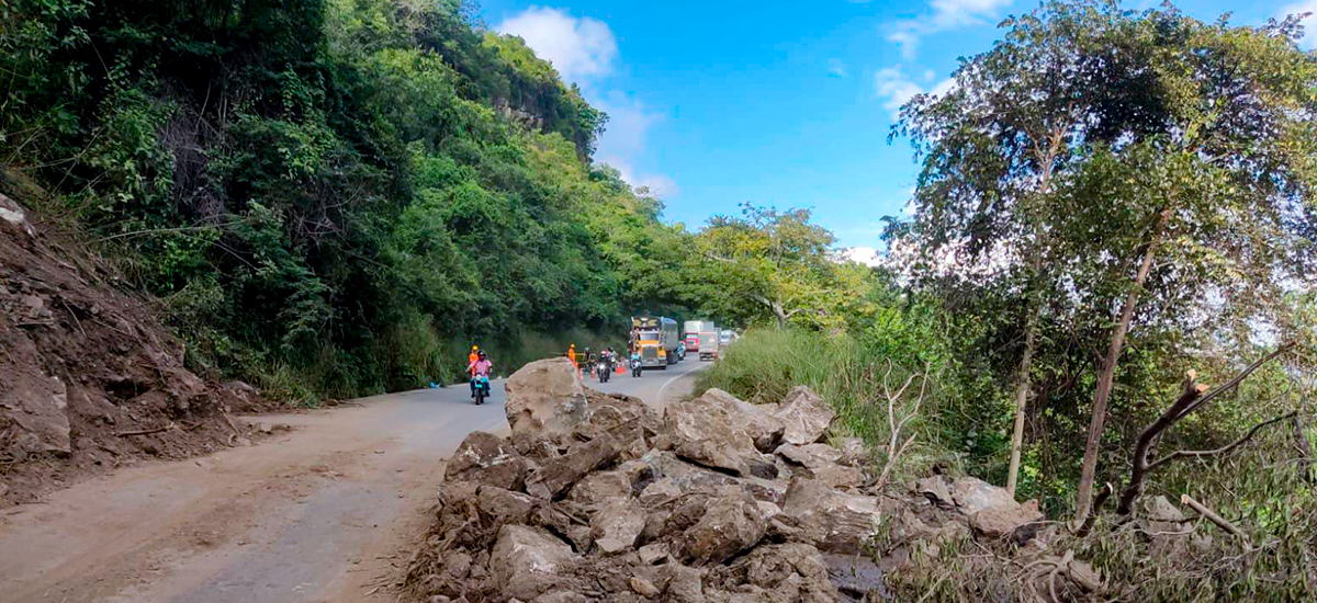 Fotografía en la que se aprecia parte del talúd de tierra en el km 117, sector El Raizón, de la vía Puente Nacional - San Gil y al fondo a personas en diferentes medios de transporte esperando para cruzar.
